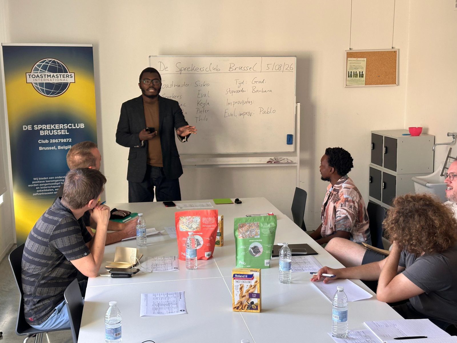 Lid van De Sprekersclub Brussel geeft een speech voor de groep, met de clubbanner op de achtergrond